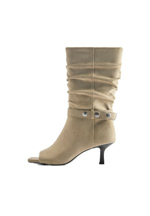 Botte beige en daim mi-mollet avec tige souple, bride décorative avec boutons argentés, bout ouvert et talon kitten noir fin.