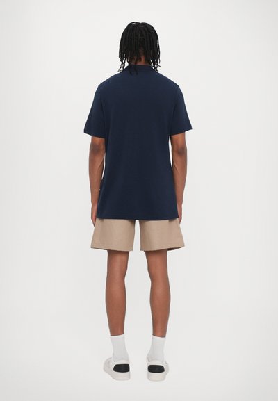 Camiseta azul marino de manga corta, combinada con pantalones cortos beige. La camiseta tiene un corte holgado y textura lisa; los pantalones cortos son de longitud hasta la rodilla.