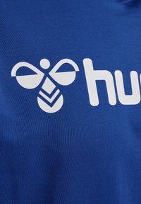 Blå bomullströja med en stor vit logotyp som har en stiliserad bi-design och texten "hub" i fet, modern stil.