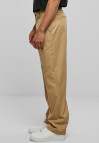 Khaki trousers made of smooth fabric with a straight-leg design, featuring a side pocket and worn with white sneakers.