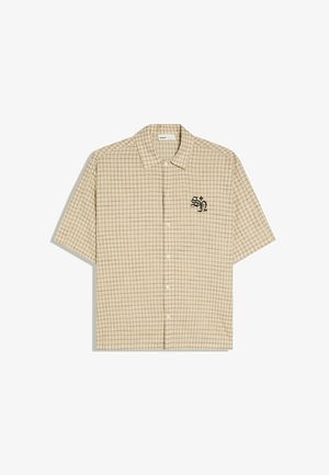 Beige overhemd met korte mouwen en knopen, met een dun bruin geruit patroon en zwarte geborduurde "SN" letters op de linkerborst.