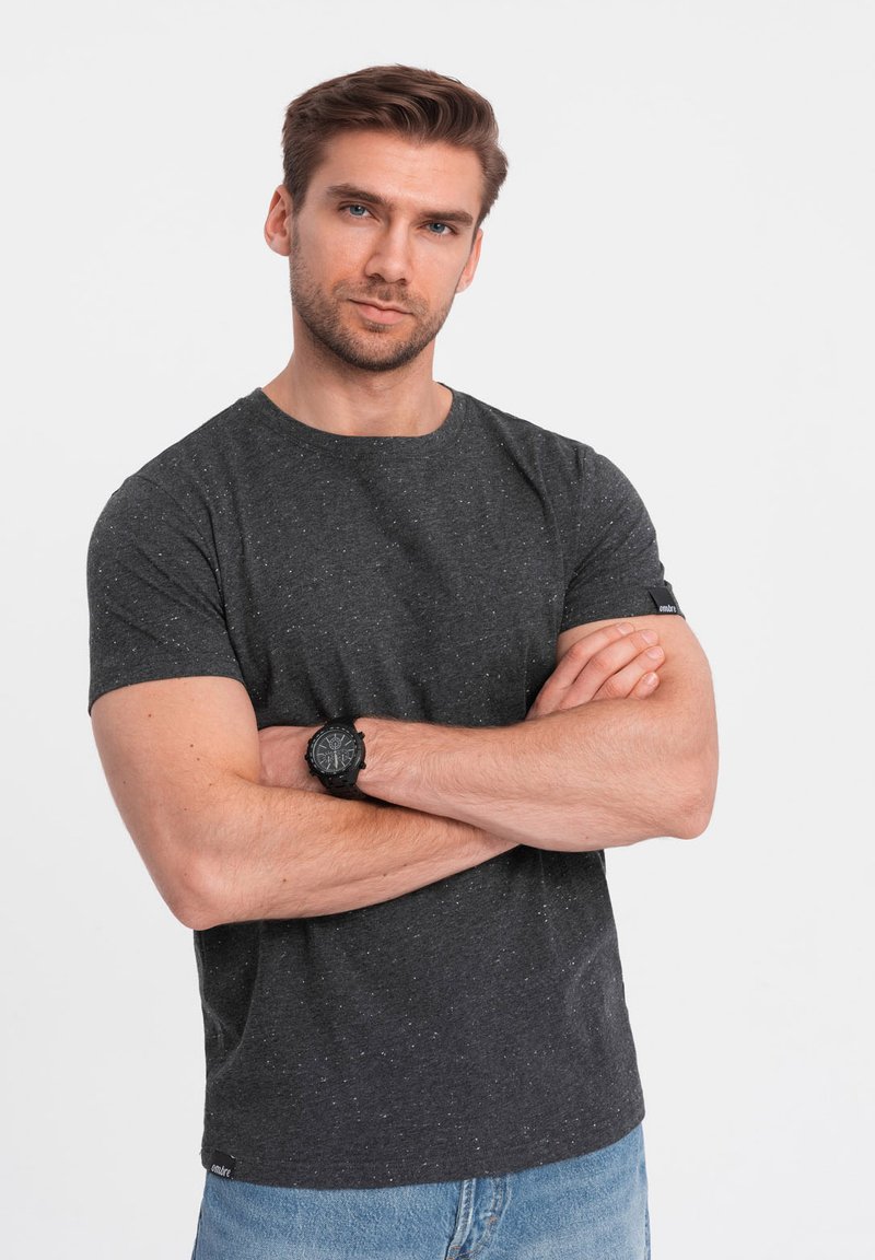 Gråprikket t-shirt med rund halsudskæring, korte ærmer og et sort mærke i kanten. Båret med blå denim jeans.