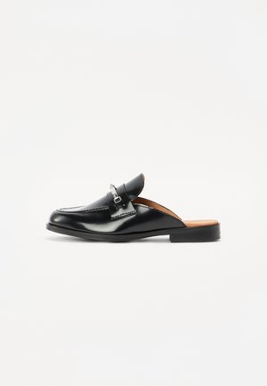 Scarpa nera in pelle senza lacci con punta arrotondata, cuciture dettagliate e un accento in metallo argentato. Suola piatta con effetto legno all'interno.