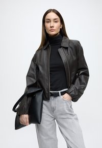 Barna bőr bombázó kabát, fekete garbó, világosszürke farmer és fekete kézitáska. Sima textúra, strukturált kialakítás és testhez simuló megjelenés.