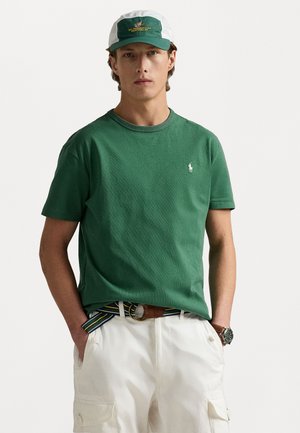 Green cotton T-shirt with a crew neckline and short sleeves, paired with white cargo shorts and a green and white cap featuring text.