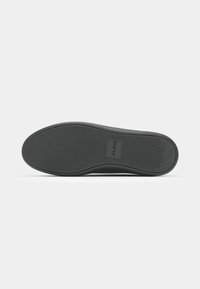 Black rubber shoe sole with a textured pattern, featuring a slight curve and a logo in the center. Flat and round shape.