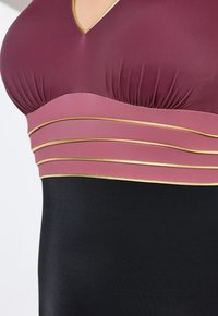 Maillot de bain bordeaux et noir avec un décolleté en V, une bande rose superposée avec des accents dorés, et une texture lisse et extensible.