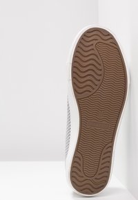 Valkoiset tennarit, joissa on harmaasta kudotusta materiaalista valmistettu teksturoitu yläosa, kumipohja, jossa on aaltoileva kuvio, ja ruskeat brändäys yksityiskohdat pohjassa. Koko 37.