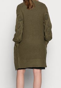 Olivově zelený pletený cardigan s volným střihem, detaily krajkových rukávů a bočními kapsami. Texturovaný materiál s žebrovaným lemem.