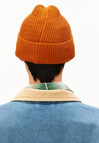 Orange knit beanie with a ribbed texture, shown from the back, resting on dark hair. Worn with a denim jacket and plaid shirt underneath.