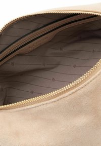Interior de bolso de ante beige con una textura suave, con un cierre dorado y forrado con un patrón geométrico en tonos sutiles.