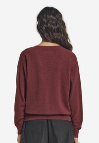 Bordeauxfarbener Wollpullover mit lockerer Passform, überhängenden Schultern, gerippten Bündchen und Saum. Glatte Textur ohne sichtbare Muster oder Hardwaredetails.