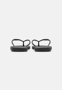 Chinelas pretas com solas texturizadas e tiras finas e curvadas. As tiras são planas e ligeiramente flexíveis, proporcionando um design simples com detalhe mínimo.