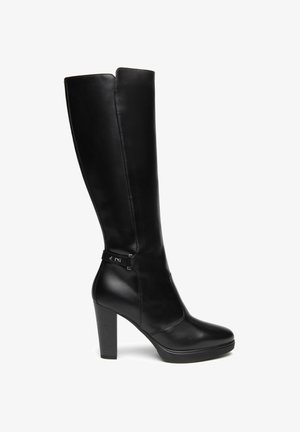 Bota alta negra de cuero para mujer con tacón alto y grueso y una correa decorativa cerca del tobillo, vista de lado sobre un fondo blanco.
