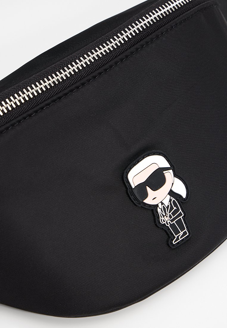 Sac banane en nylon noir avec une fermeture éclair argentée et un patch d'icône de designer en noir et blanc de style cartoon sur le devant.
