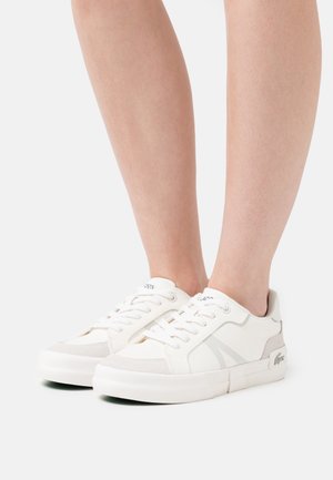 Zapatillas de tela blanca con detalles en gris, suela de goma, punta redonda y diseño con cordones que presenta el logo en la lengüeta y en el lateral.