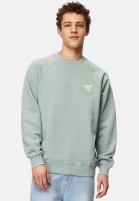 Vaaleanvihreä huppari pyöreällä kaula-aukolla, resorit hihoissa ja helmassa. Vasemmassa rinnassa on pieni valkoinen logo. Pehmeä, teksturoitu kangas.