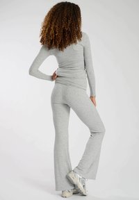 Haut gris à manches longues et pantalon évasé en matériau doux et extensible. Le pantalon a une taille ajustée et est de longueur cheville avec une texture lisse.