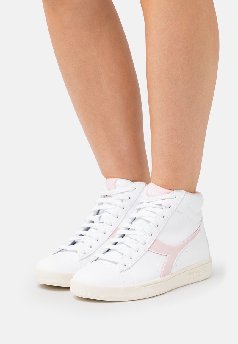 Kotníkové tenisky z bílého syntetického materiálu s růžovými akcenty, mají hladký povrch, kulatou špičku a tradiční zavazování na tkaničky.