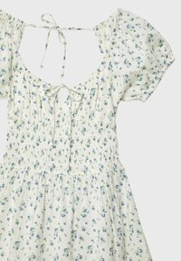 Robe blanche à imprimé floral bleu, manches courtes bouffantes, taille smockée, détails à nouer devant et derrière, et encolure carrée.