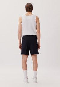 Top in maglia bianca, pantaloni navy a pletti e sneakers bianche. I pantaloni presentano tasche a toppa con chiusure a bottone. Design semplice.