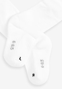 Chaussettes en mélange de coton blanches avec une texture côtelée, portant des marquages de taille "G" et "D" en noir sur les semelles. Finition lisse sans motifs.
