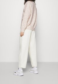 Felpa a fantasia floreale in rosa pallido, abbinata a pantaloni palazzo bianchi e sneaker bianchi, che mostrano una vestibilità comoda e uno stile casual.