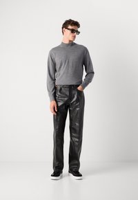 Šedý svetr s vysokým límcem, černé kožené kalhoty a černé tenisky s bílou podrážkou. Úzký střih, hladká textura a minimalistic design.