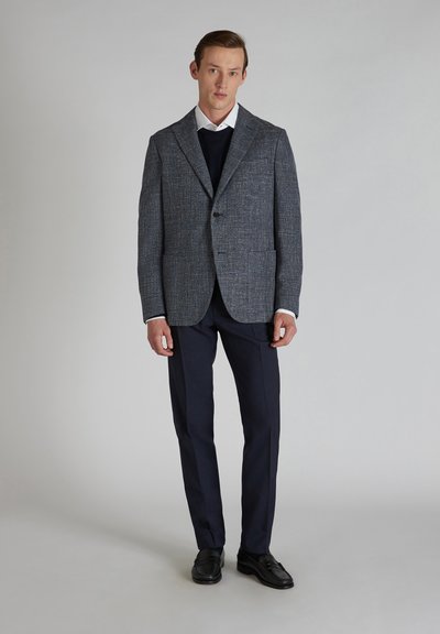 Grau strukturiertes Blazer mit Reverskragen, einreihigem Knopfverschluss und zwei vorderen Taschen, kombiniert mit dunklen Hosen und schwarzen Schuhen.