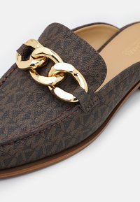 Diéthique en cuir marron avec texture à motifs et détail en chaîne dorée. Présente une pointe arrondie et une couture contrastante le long des bords.