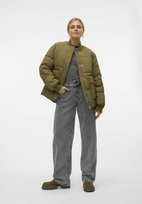 Olijfgroene pufferjack met een geribbelde kraag, gestreepte top eronder, grijze wijde jeans en groene instappers met een stevige zool.