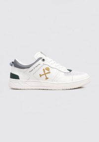 Zapatilla blanca con detalles grises y lengüeta en el talón verde. Cuenta con un logo cosido, puntera perforada y suela texturizada para mejor agarre.