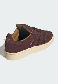 Suede sneakers in dark burgundy with beige rubber sole, featuring five eyelets, embossed logo, and padded collar for comfort.