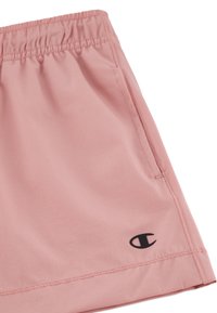 Shorts de sport rose clair avec une taille élastique, ornés d'un logo noir sur le bas à gauche et d'un tissu lisse et texturé.