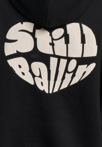 Czarny kaptur z dużym, zakrzywionym białym napisem "Still Ballin" z motywem serca. Gładka bawełniana tekstura.