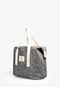 Torba typu tote w leopardzi wzór, wykonana z trwałego materiału, z beżowymi uchwytami, zieloną łatą z logo i bezpiecznym zapięciem bocznym.