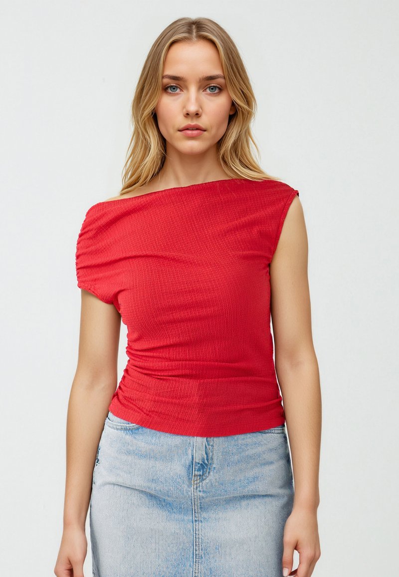 Czerwony, prążkowany top typu off-shoulder z krótkimi rękawami, z falbanami w okolicy talii. W zestawie ze jasnoniebieską spódnicą dżinsową.