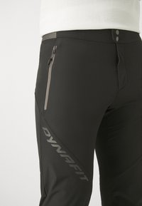 Zwarte sportbroeken met een ritszak, een slank ontwerp met een reflecterend logo en een gladde, rekbare stof.