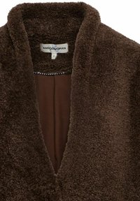 Bruine nepbonten ochtendjas met een zachte textuur, een reverskraag en een V-hals ontwerp. De binnenkant heeft een effen bruine voering met een klein zwart-wit ruitpatroon.