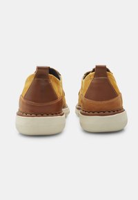 Sneaker gialle in rete con dettagli in pelle marrone, punta rotonda e suole in gomma bianca. Include un tab sul tallone per una facile calzata.