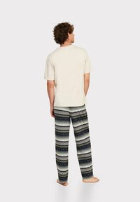 Herrencreme-T-Shirt und gemusterte Schlafanzughosen mit schwarz-weißen geometrischen Designs, die grüne Akzente und eine lockere Passform aufweisen.