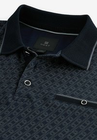 Tricou polo bleumarin cu un model spiral, guler texturat și deschidere cu două butoane, dotat cu un buzunar pe piept și etichetă cu logo.