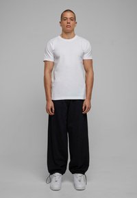 Hvid bomulds t-shirt, kortærmet; samlet med løse, sorte bukser og hvide sneakers med elastiske manchetter. Enkel, minimalistisk design.