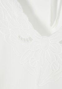Tessuto bianco con ricami floreali intricati e dettagliate cuciture. Il design include petali e foglie, arricchendo la texture e la profondità.