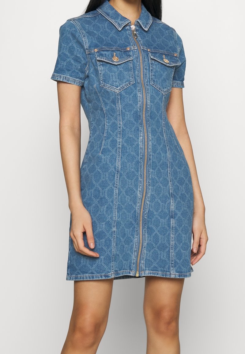 Jeansklänning med kort ärm, krage, dragkedja fram, två bröstfickor och ett geometriskt mönster i ljusblått.