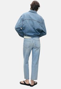 Svetlo modra jeans jakna in jeans s sproščenim krojem. Sandali imajo črno naramnico. Tkanina ima klasično prano teksturo.