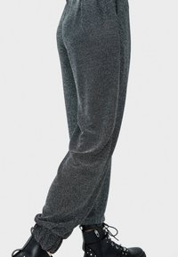 Szare, metaliczne spodnie dresowe z prążkowanym pasem i mankietami, charakteryzujące się gładką teksturą i luźnym krojem, zestawione z czarnymi butami.