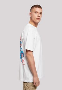 White cotton t-shirt featuring a blue and red graphic print on the back, short sleeves, and a relaxed fit.