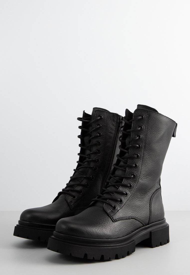 Czarne skórzane buty wojskowe z teksturowanym wykończeniem, wysoką cholewką i sznurowanym przodem. Posiadają grubą gumową podeszwę z przyczepnymi bieżnikami.