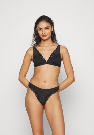 Mustmustest muströödiga bralette'il on sügav V-kaelus ja laiad rihmad. Sobiva musta stringi ääres on laineline pitsäär.